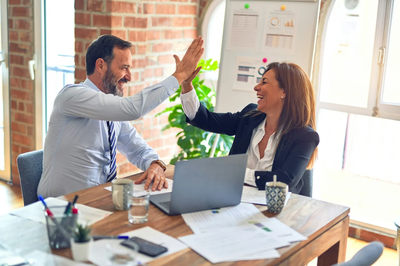 Des collègues célèbrent l'achèvement réussi d'une tâche ou d'un projet par un high-five dans un bureau.